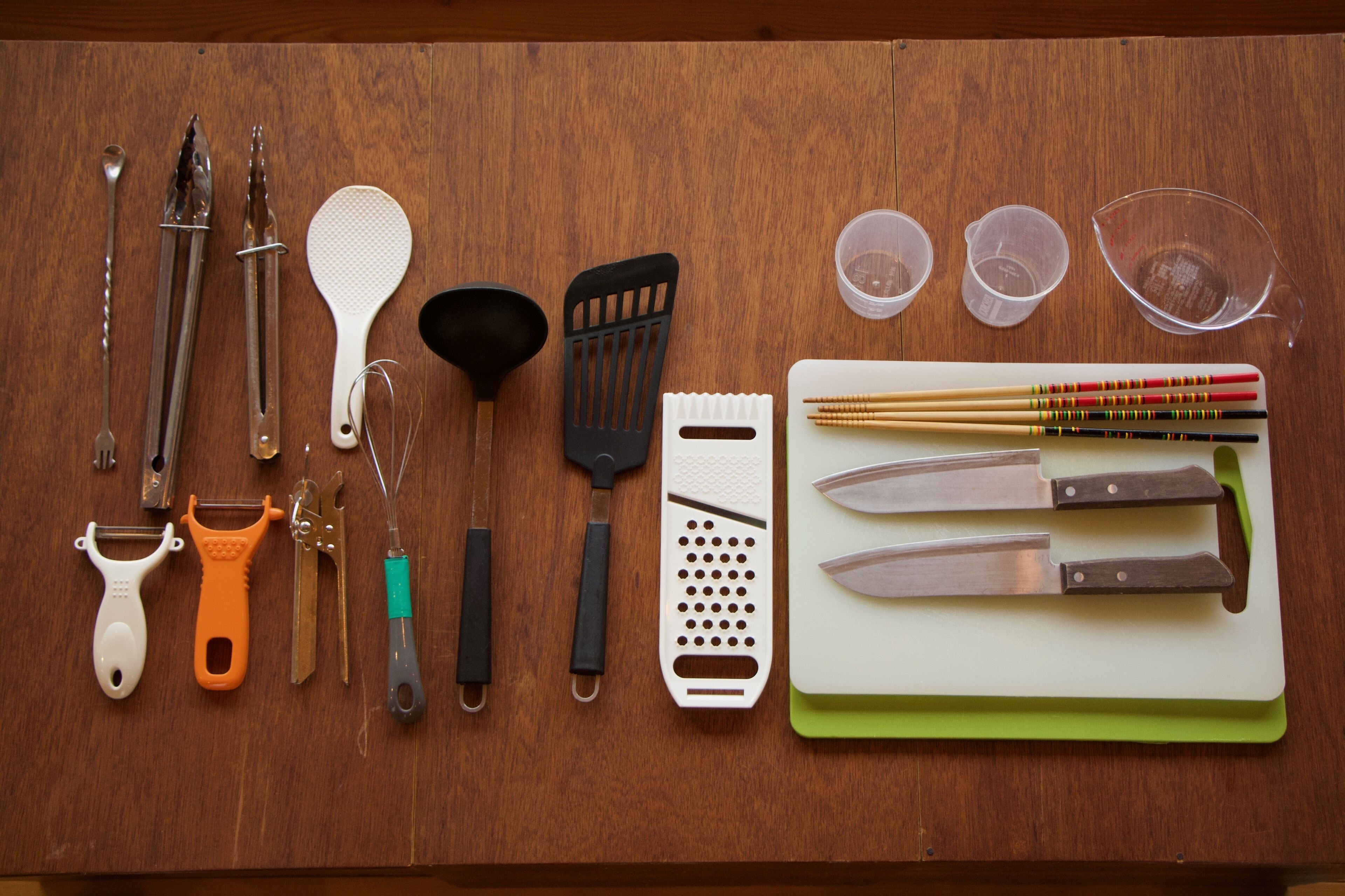 A wooden surface with various kitchen utensils and tools, including knives, a grater, and measuring cups.