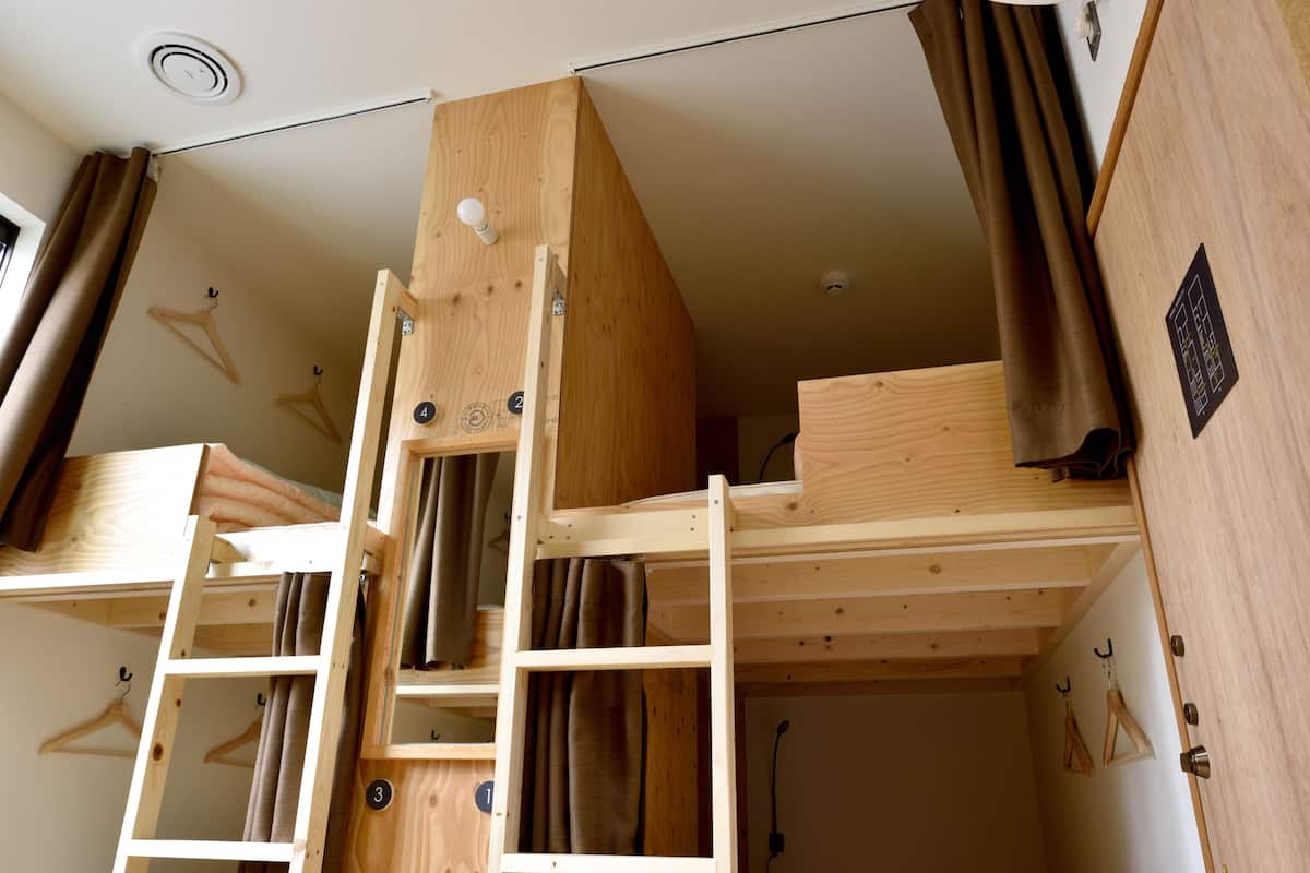 A bunk bed with a ladder, wooden walls, and a ceiling vent.