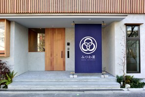 A modern building entrance with a wooden door, a blue banner with a logo, and a concrete staircase. - Hostel Mitsuwaya Osaka (Osaka)