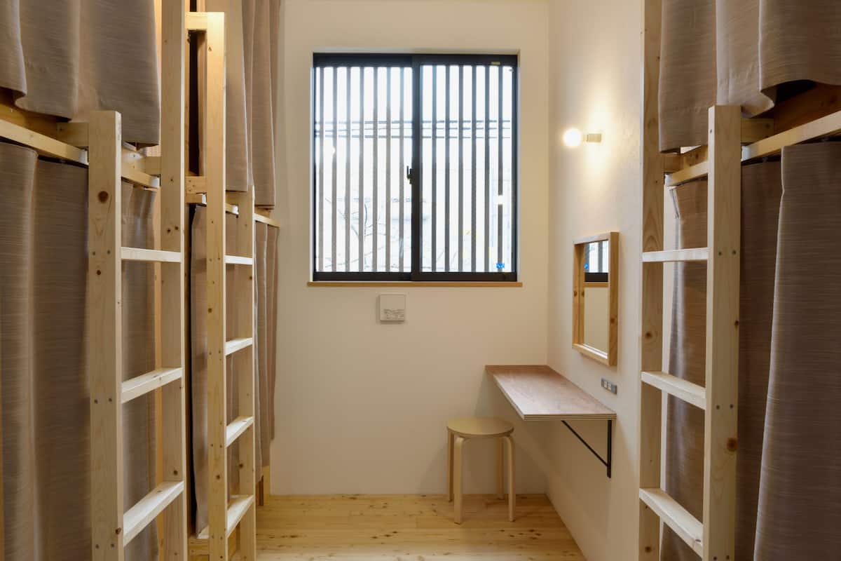 A narrow hallway with wooden shelving units, a small stool, a desk, and a window with vertical blinds.