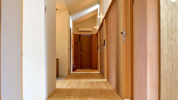 A hallway with wooden flooring and doors on both sides, leading to a room with an air conditioning unit on the ceiling.