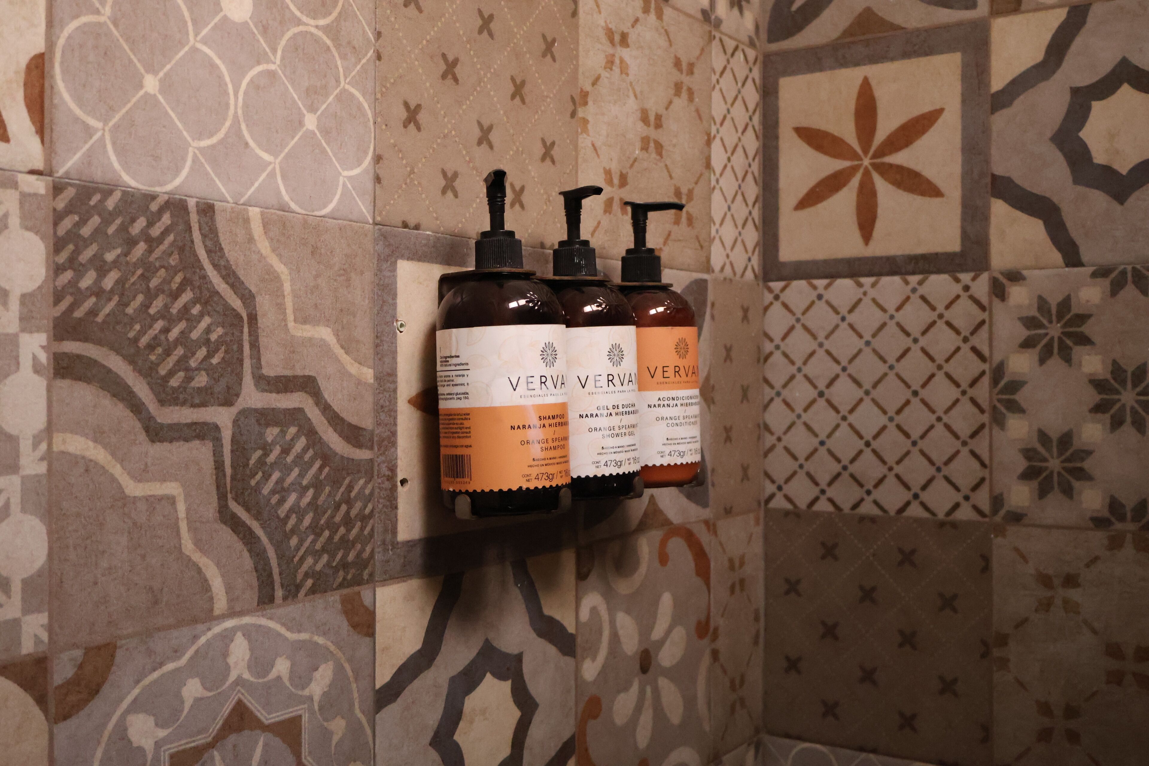 Casa de banho com azulejos estampados e três frascos de shampoo Vervy Vervy.