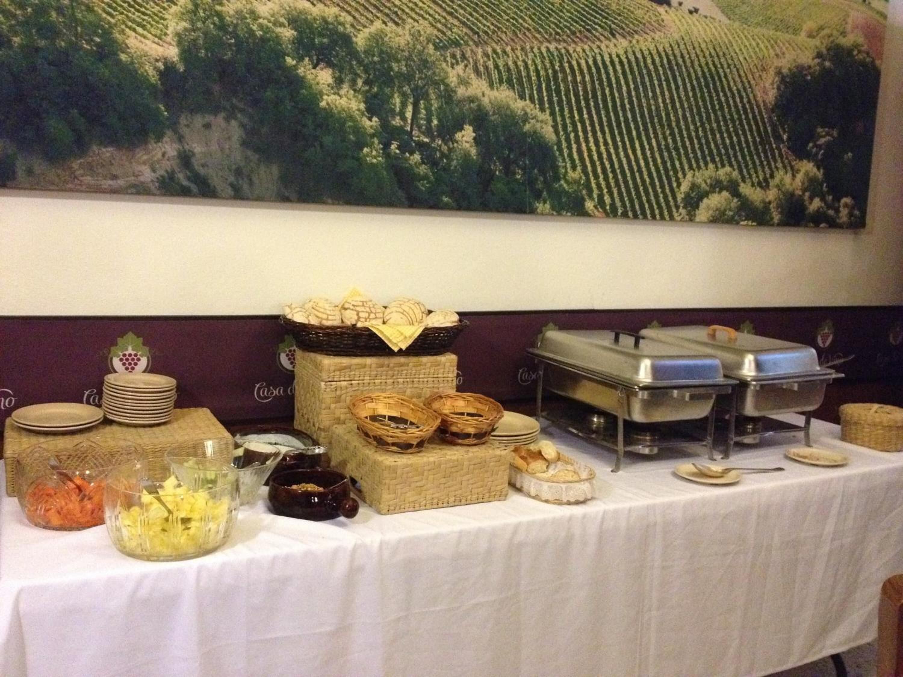 A buffet table with various food items and serving utensils, set against a backdrop of a vineyard landscape.