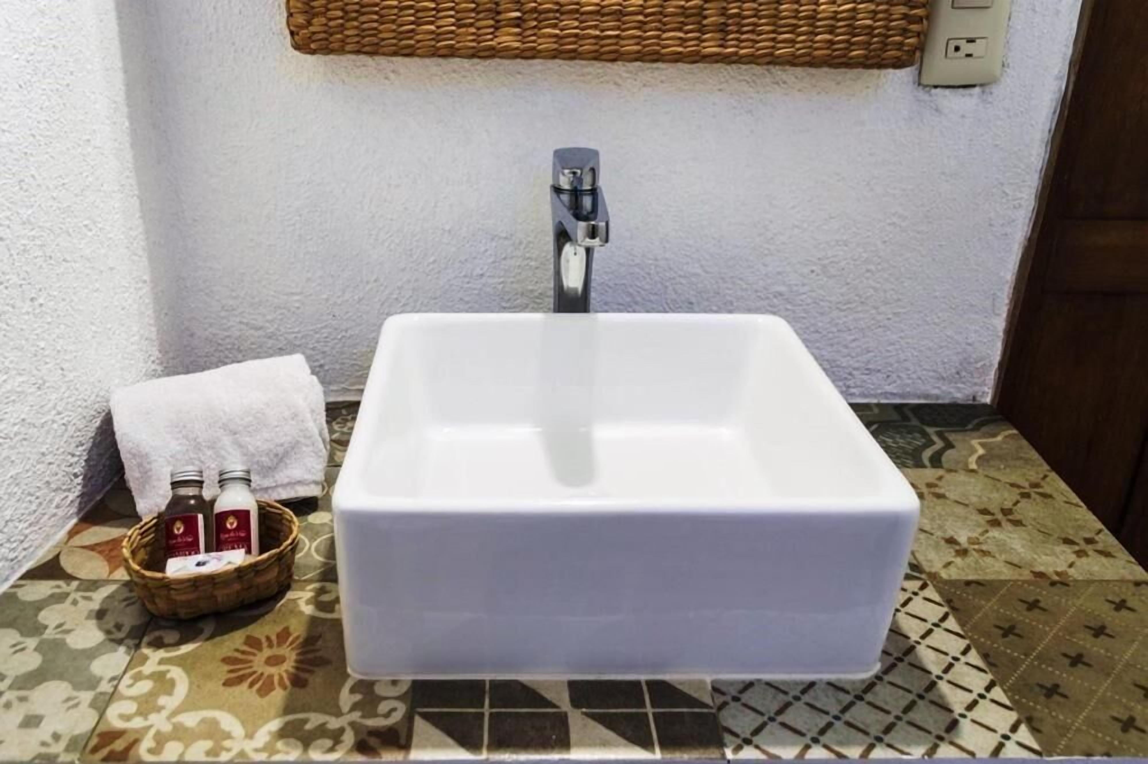Un baño con lavamanos blanco, una cesta de artículos de aseo y un suelo estampado.