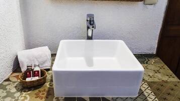 Un baño con lavamanos blanco, una cesta de artículos de aseo y un suelo estampado.