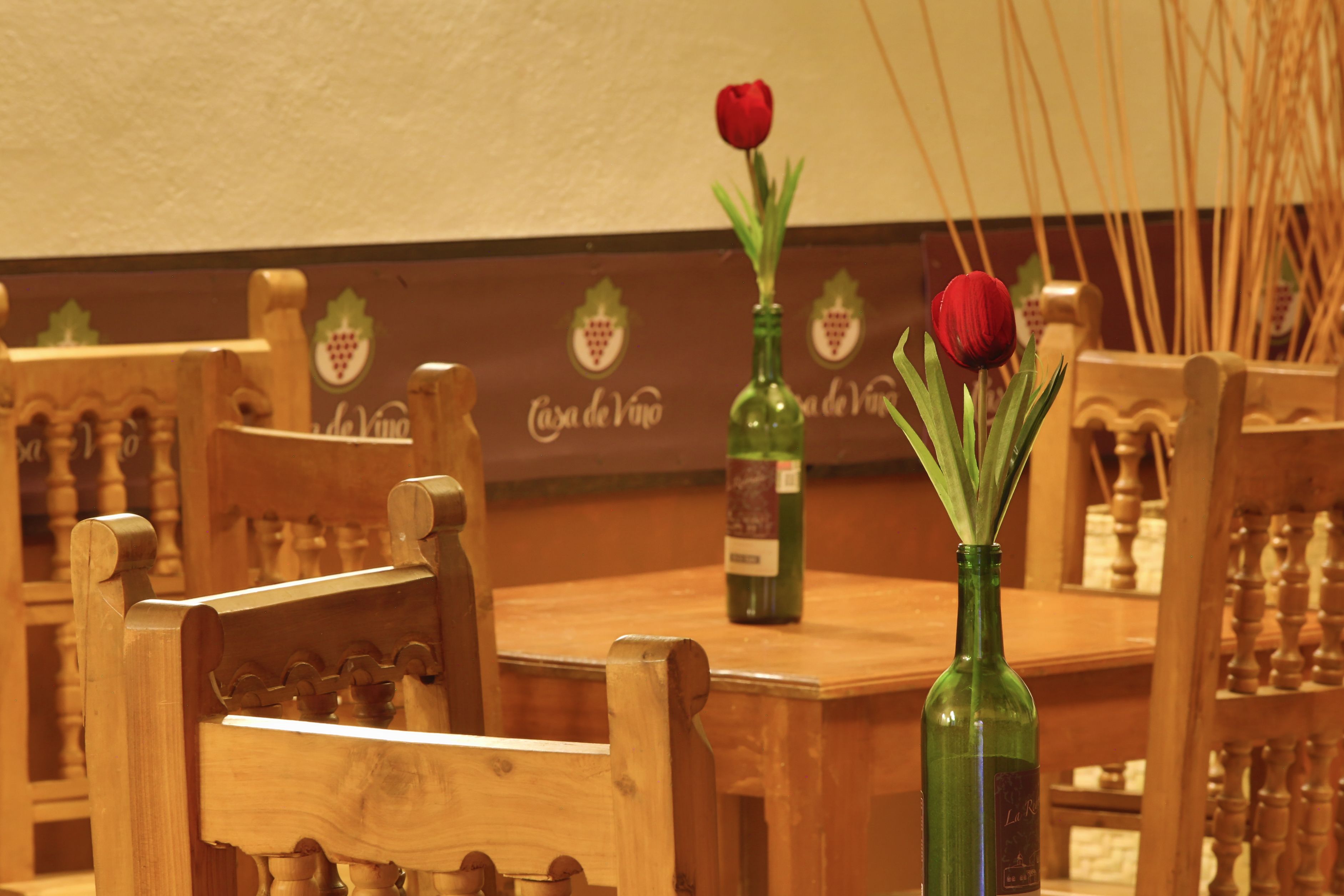 Una mesa de madera con dos botellas verdes y dos rosas rojas.