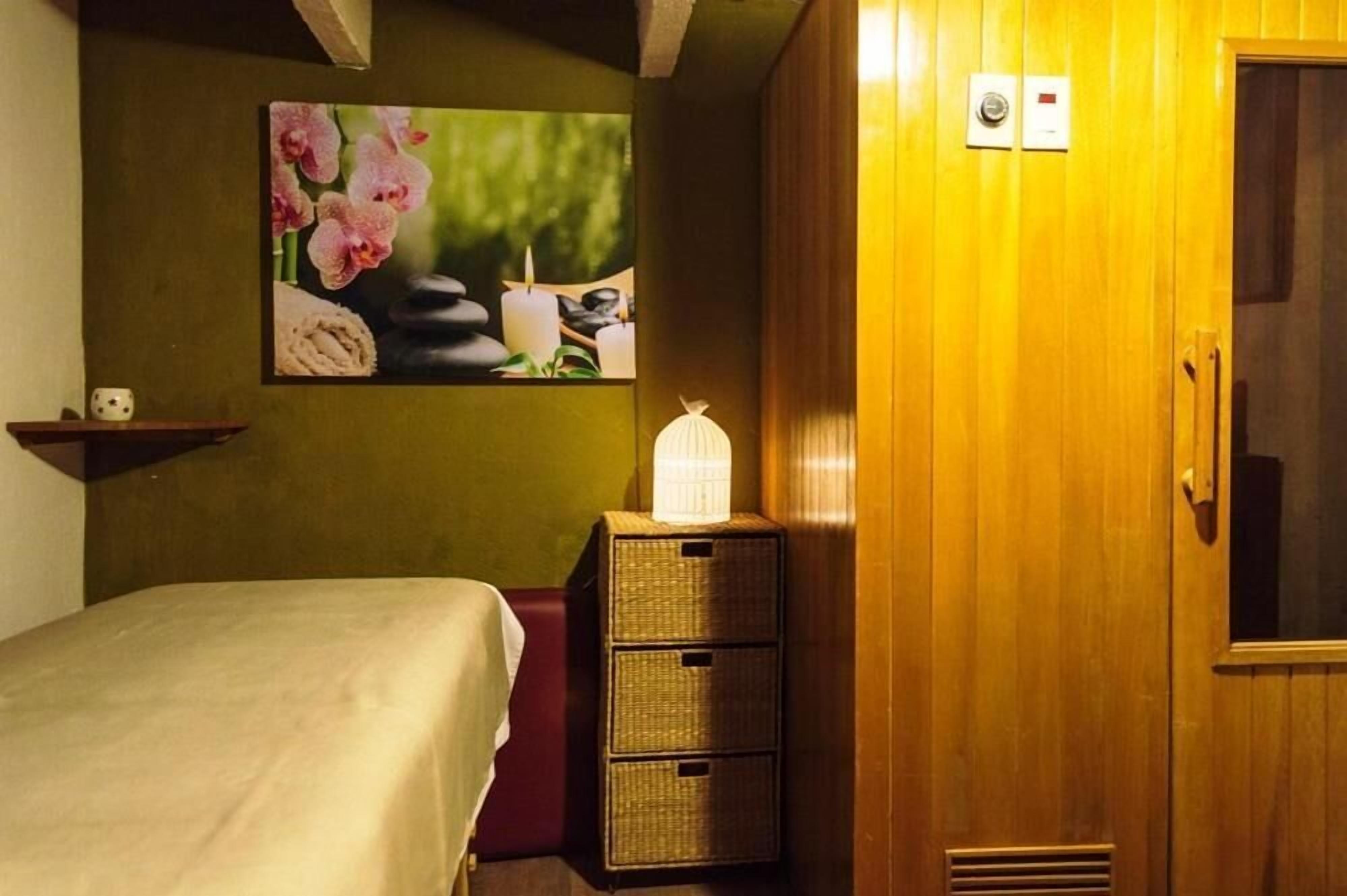 A hotel room with a bed, a wall-mounted picture of flowers and stones, a bedside lamp, and a wooden wardrobe.