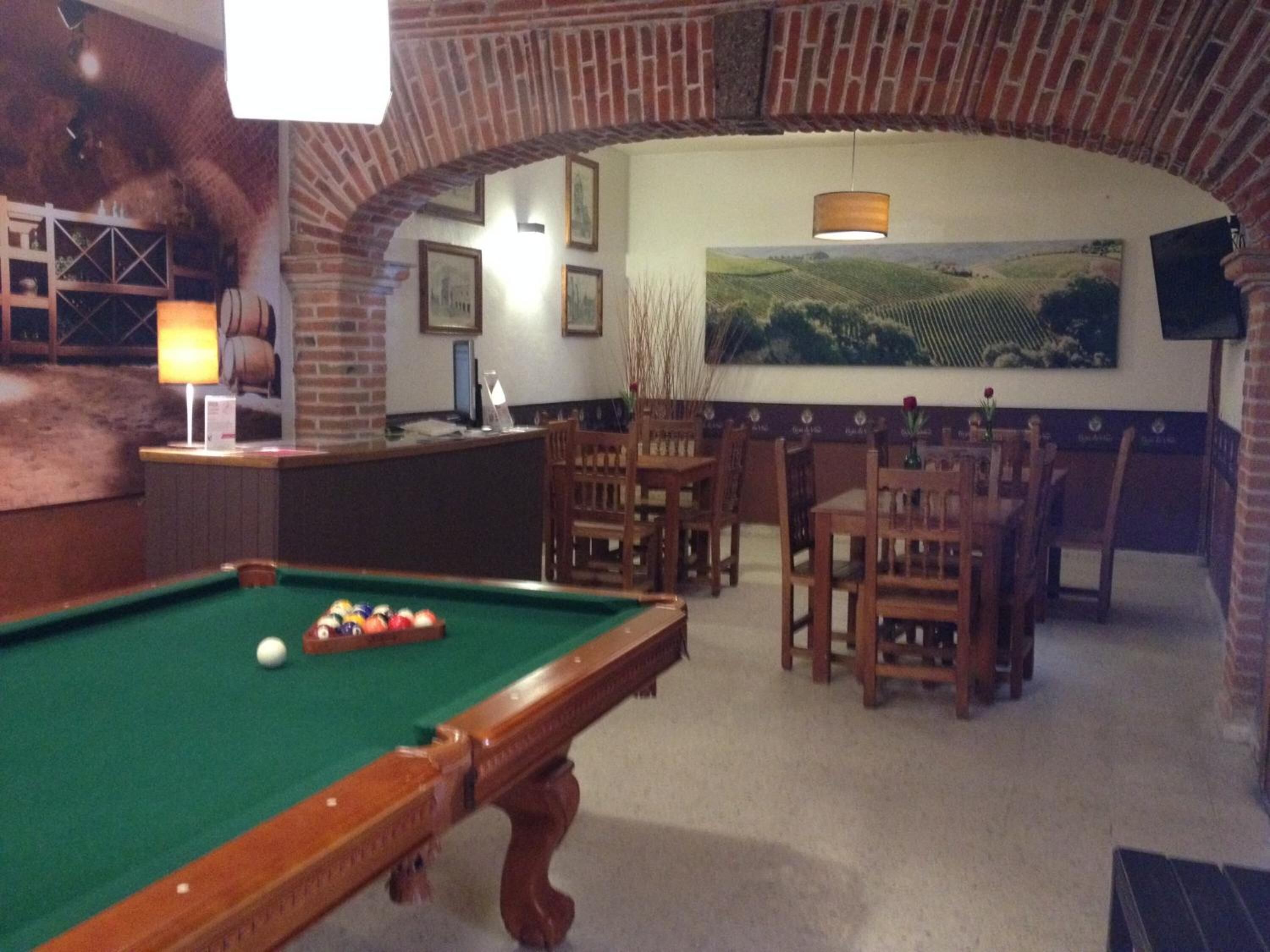 Una sala biliardo con tavolo da biliardo, sedie in legno, un'area bar e un grande dipinto paesaggistico appeso alla parete.