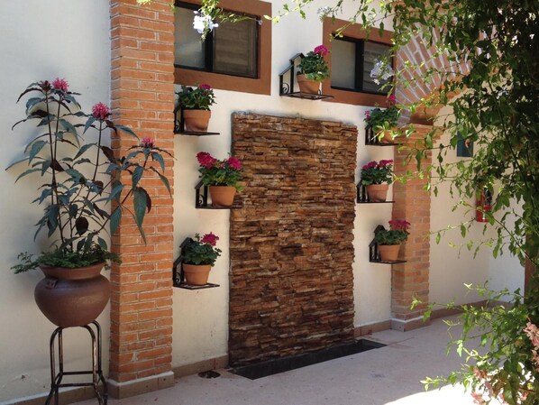 Une façade d’immeuble avec un mur en pierre, des colonnes en briques et de nombreuses plantes en pot.