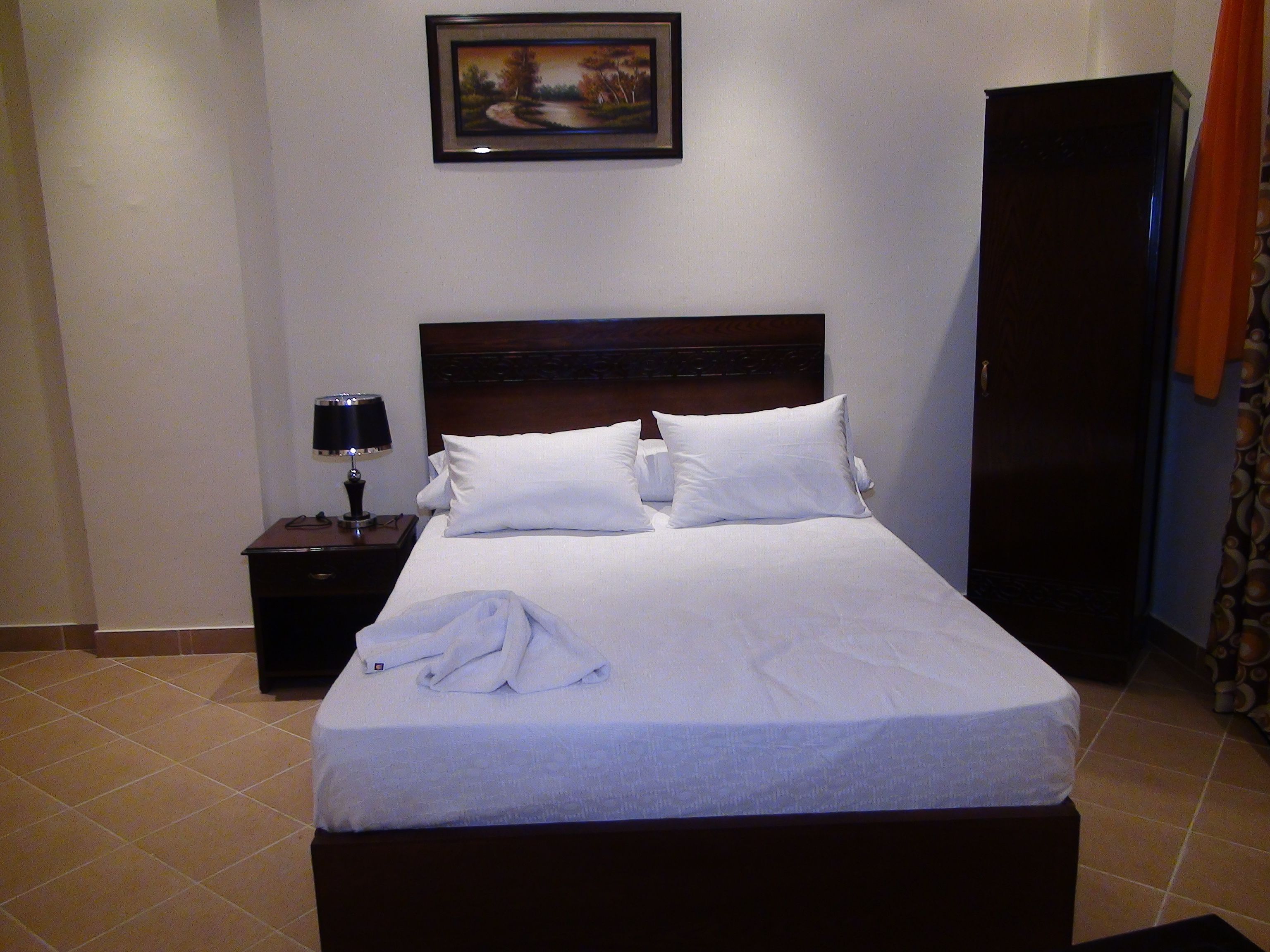 A hotel room with a bed, a nightstand, a lamp, a wardrobe, and a framed picture on the wall.