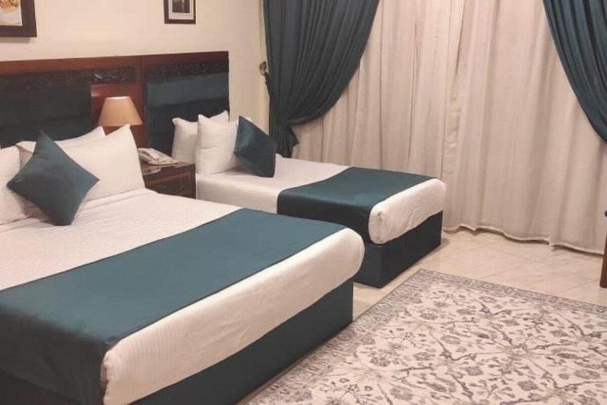 A hotel room with two beds, a nightstand, a chair, and a patterned rug.