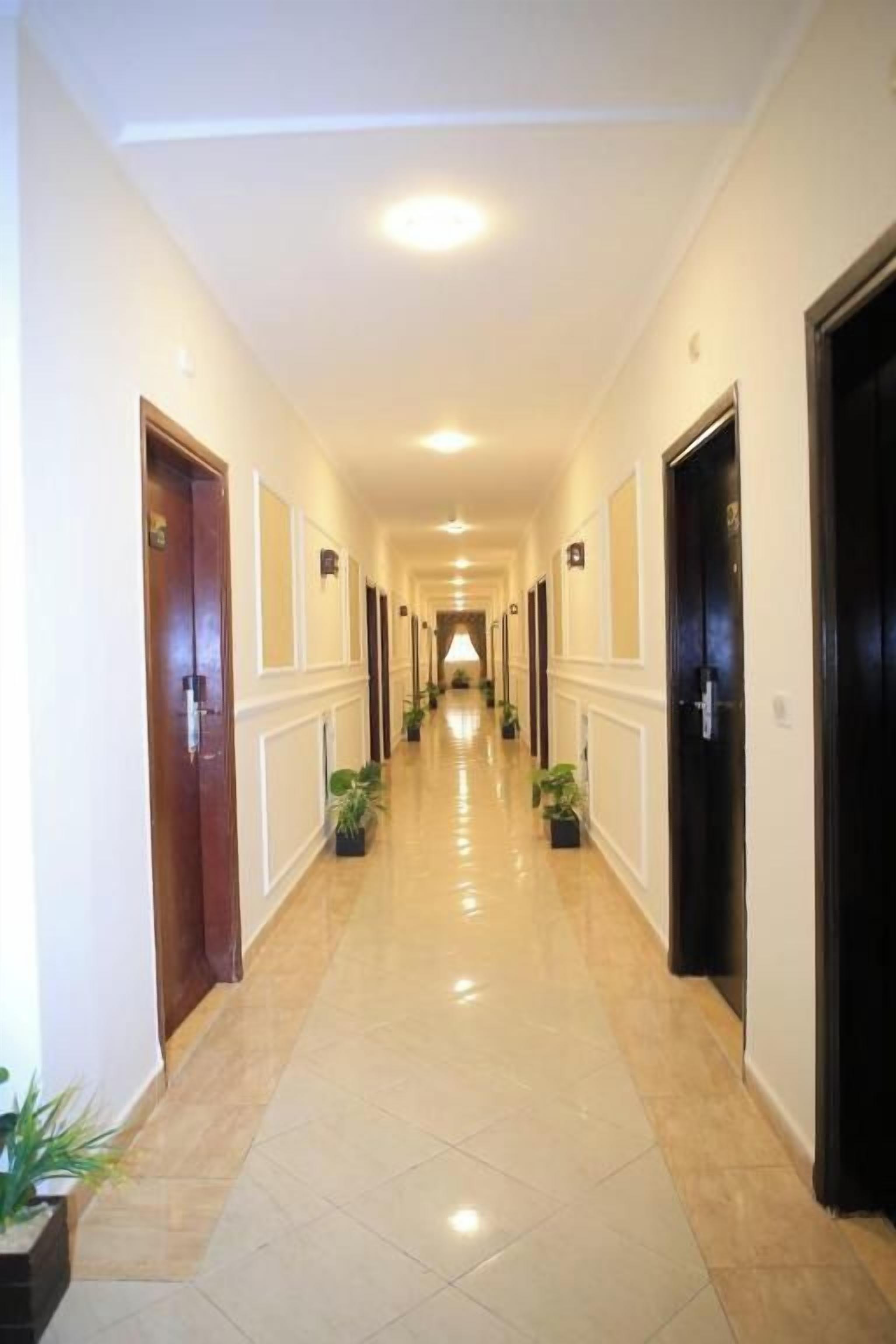 A hotel corridor with doors on both sides, potted plants, and a tiled floor.