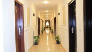 A hotel corridor with doors on both sides, potted plants, and a tiled floor.