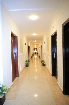 Un pasillo de hotel con puertas a ambos lados, plantas en macetas y piso de baldosas.