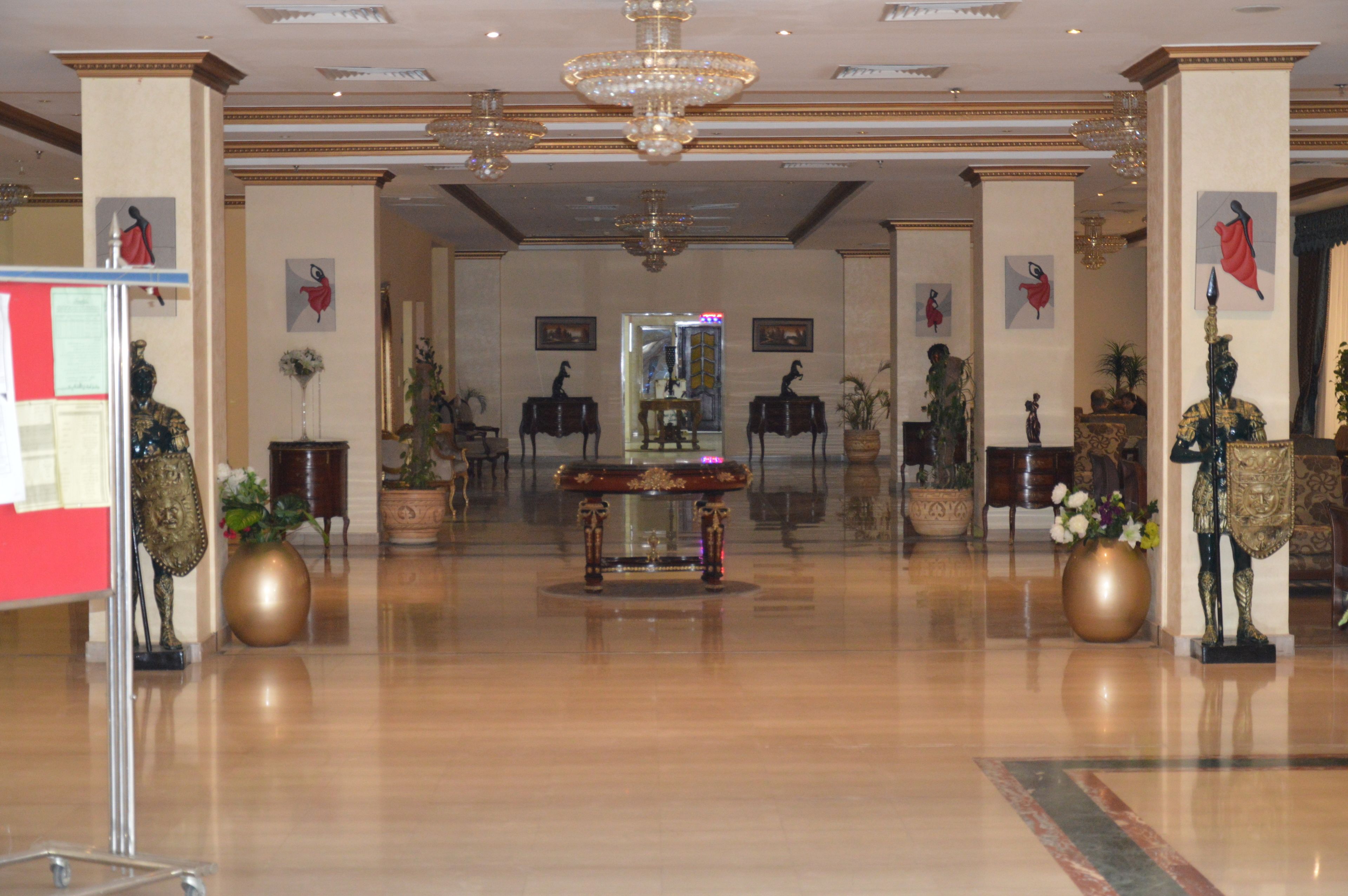 A spacious lobby with a central ornate table, potted plants, and classical statues.