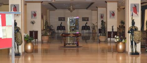A spacious lobby with a central ornate table, potted plants, and classical statues.