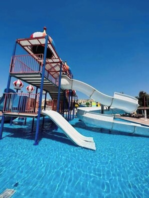 Un parque acuático con una estructura de juego de varios niveles y toboganes sobre una piscina azul cristalina.