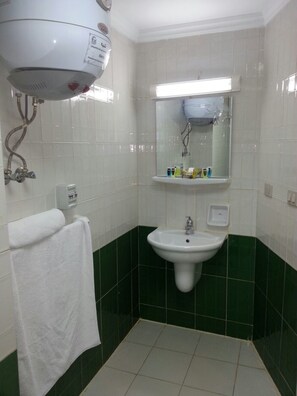 A bathroom with a white sink, green-tiled walls, a towel hanging on the wall, and a ceiling-mounted water heater. - Glorious Hotel (Cairo)
