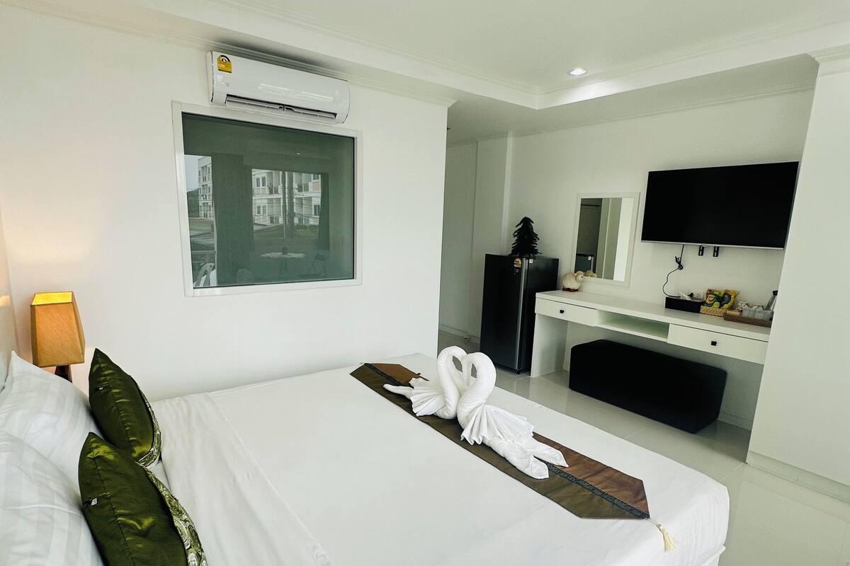 A modern hotel room with a large bed, a flat-screen TV, a built-in desk, and a window with a view of buildings.