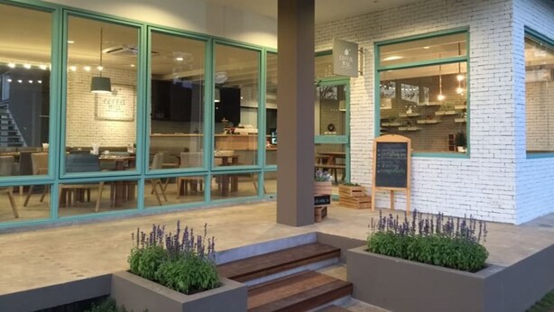 Un café moderne avec de grandes baies vitrées, une façade en briques et des places assises à l’extérieur.