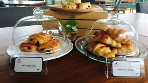 Une table présente deux présentoirs en verre recouverts de cloches, chacun contenant des pâtisseries. L’un est étiqueté « Pain au chocolat » et l’autre « Croissant fait maison ».