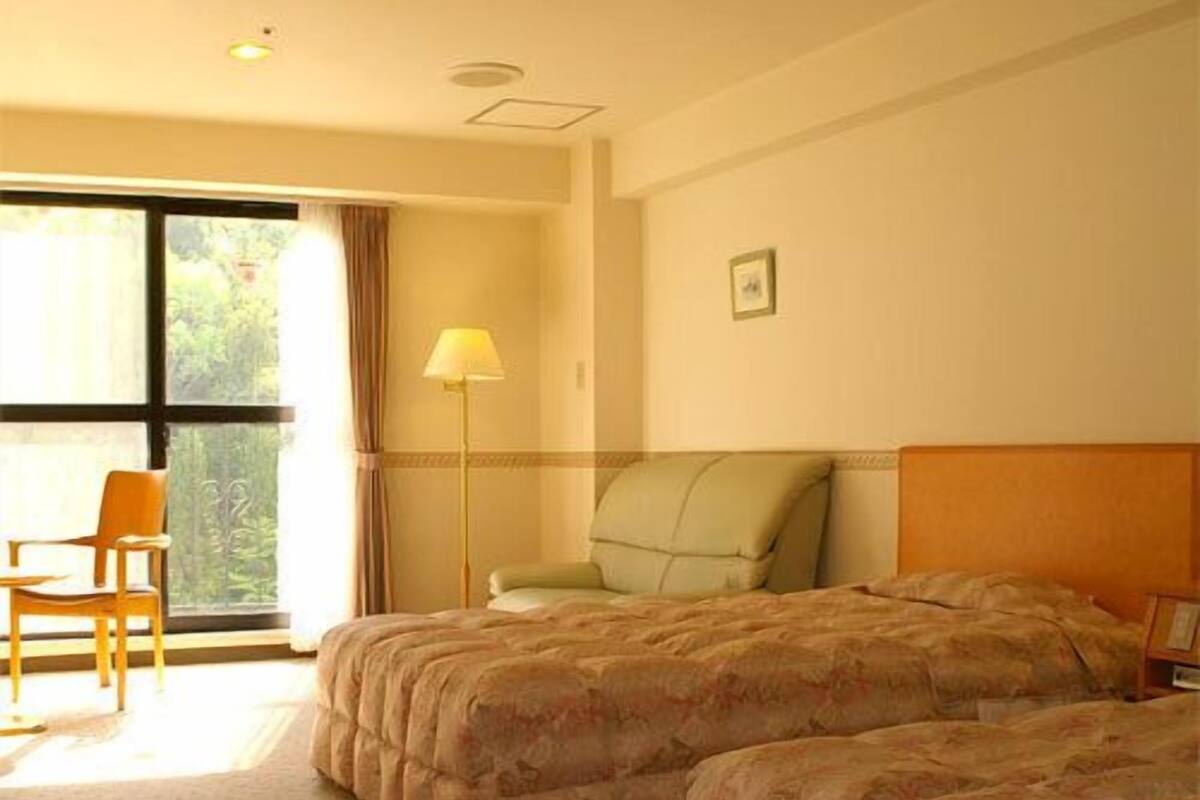 A hotel room with two beds, a chair, a lamp, and a window with curtains.