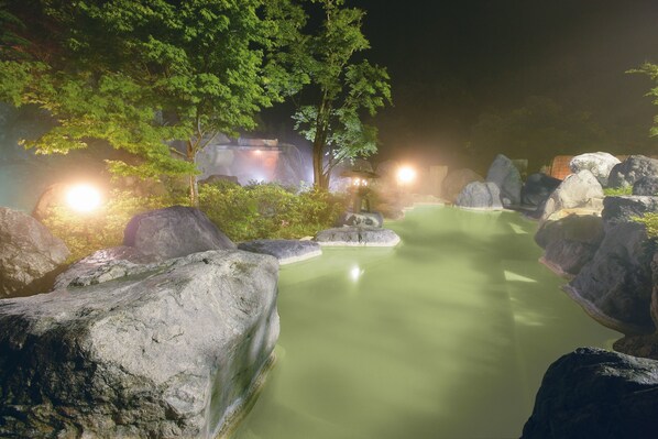 A serene outdoor setting with a hot spring surrounded by large rocks and lush greenery.