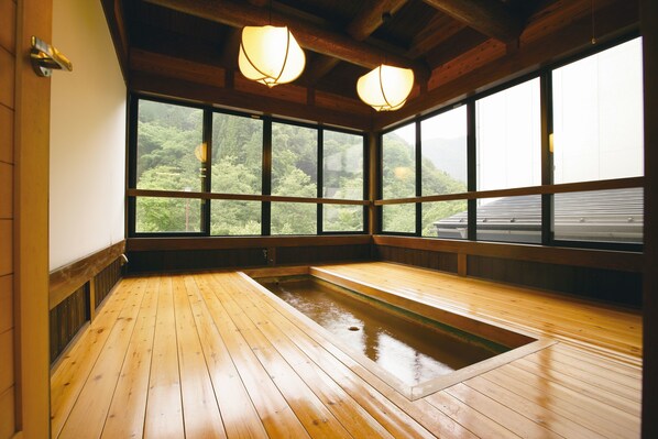 Een traditioneel Japans onsen met houten vloeren en grote ramen, met uitzicht op weelderige groene planten.