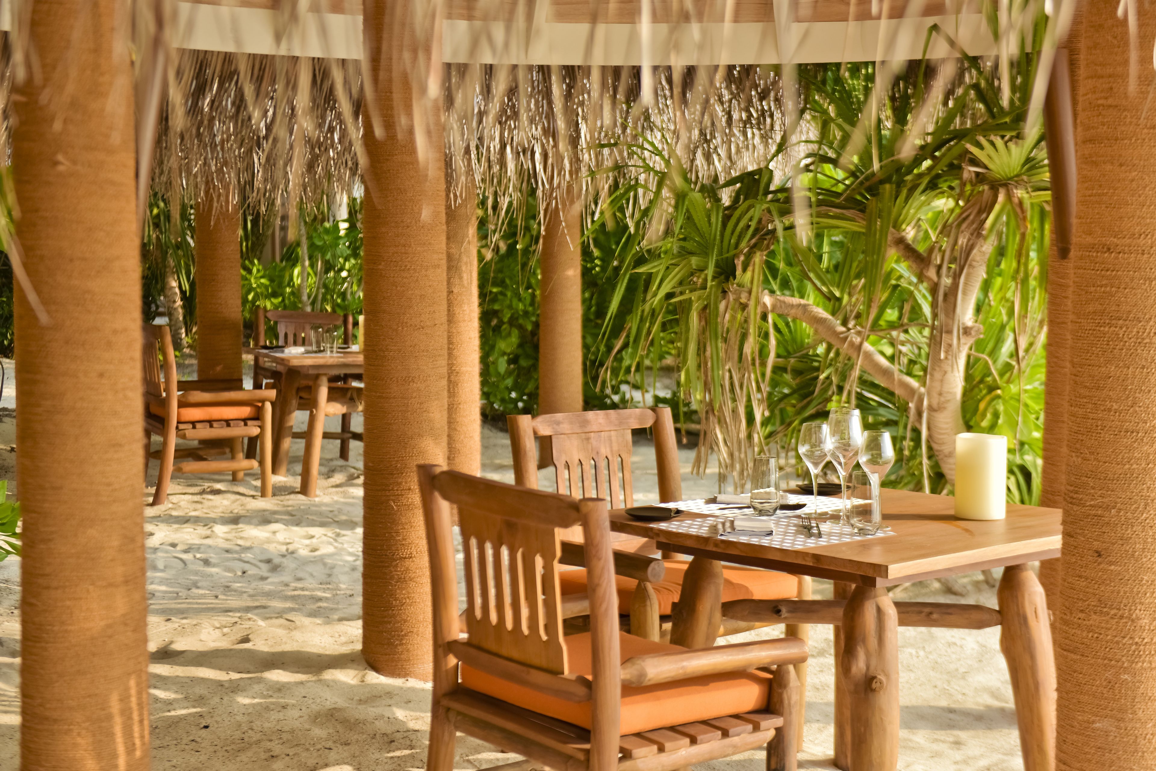 A wooden table set for dining with chairs, a candle, and a tropical backdrop.