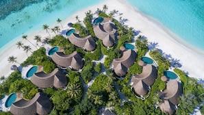 Vista aérea de un resort con estructuras de techo de paja, piscinas y palmeras.