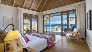 Un dormitorio amplio con una cama grande, una mesita de noche, una lámpara y vistas a la playa y al océano a través de puertas correderas de vidrio.