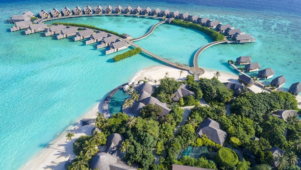 Vista aérea de un resort con bungalows sobre el agua, una piscina central y una zona de playa.