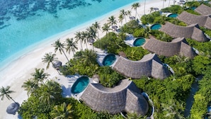 An aerial view of a resort with overwater bungalows, clear turquoise waters, and a sandy beach.
