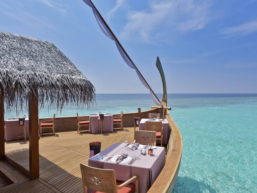 A wooden deck with tables and chairs, overlooking a clear turquoise sea.