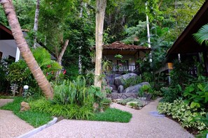 A lush garden with a thatched-roof structure, surrounded by various tropical plants and a stone pathway. - KiriRaya (Krabi)