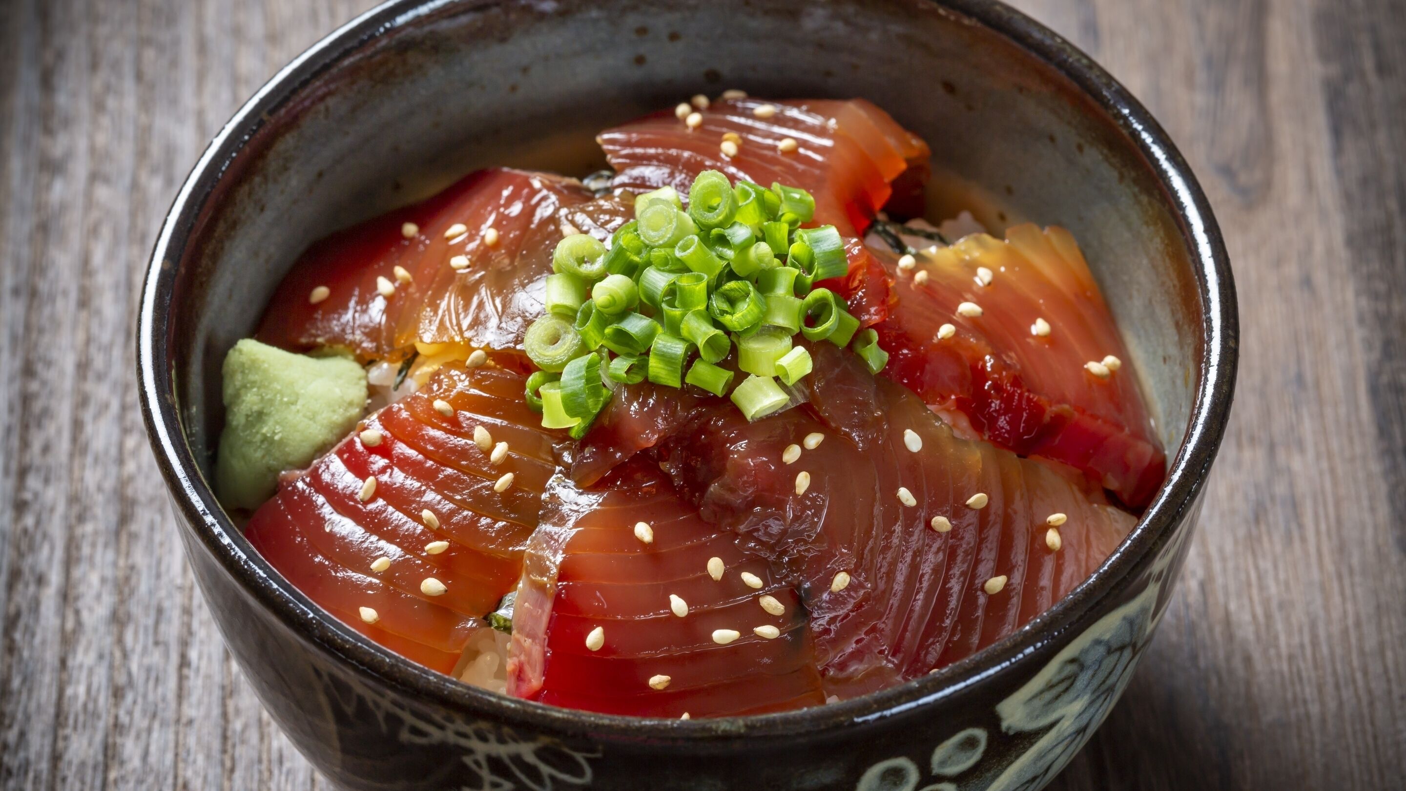 A bowl of sashimi with sesame seeds and green onions.