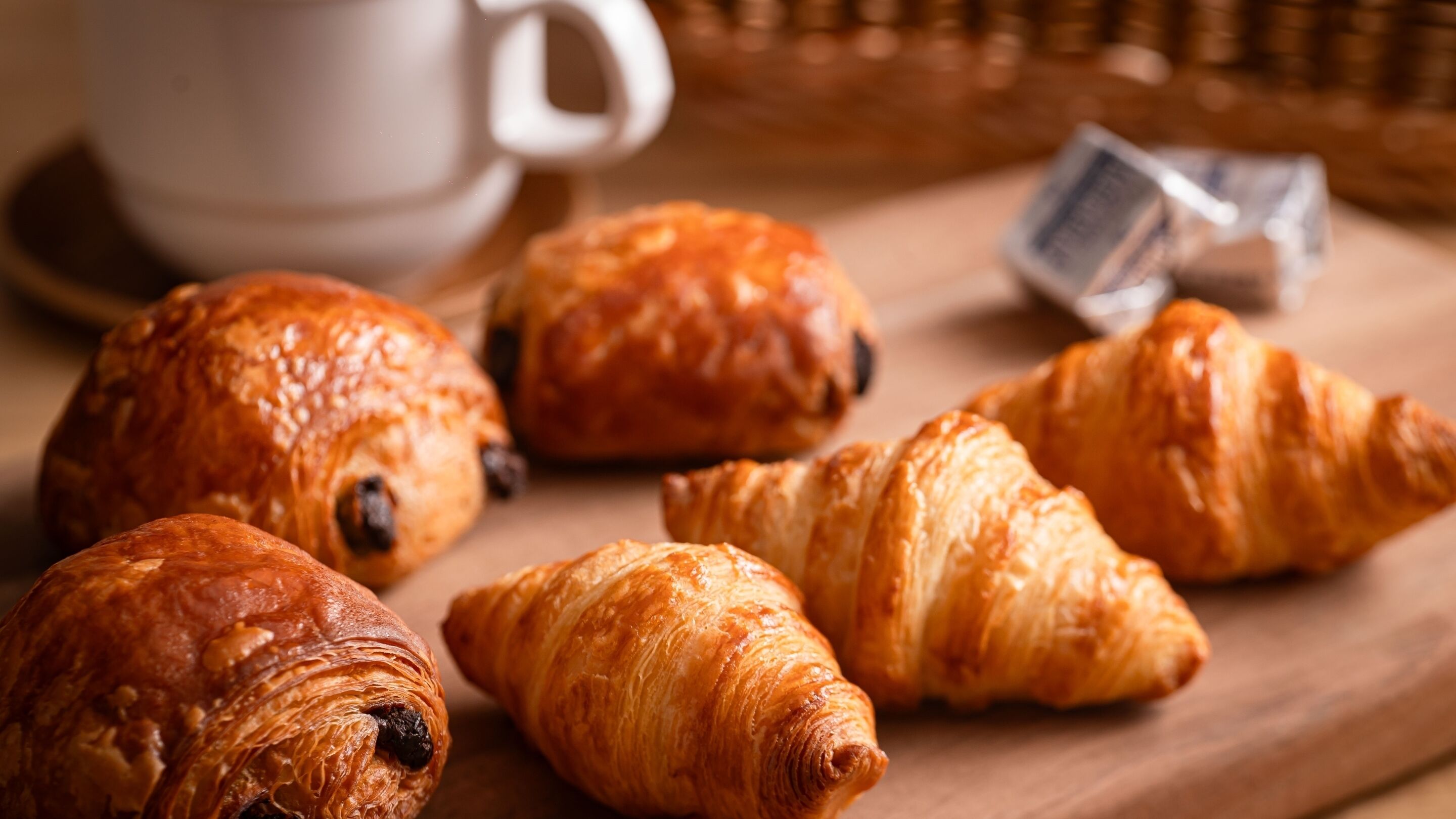 Croissants on a wooden board with a white mug in the background.