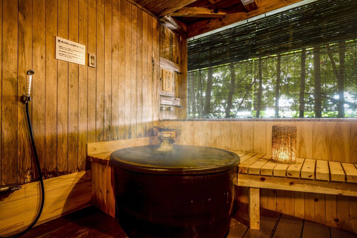 Perinteinen puinen sauna, jossa on suuri poreallas, puinen penkki ja ikkuna, josta avautuu näkymä puita kohden.