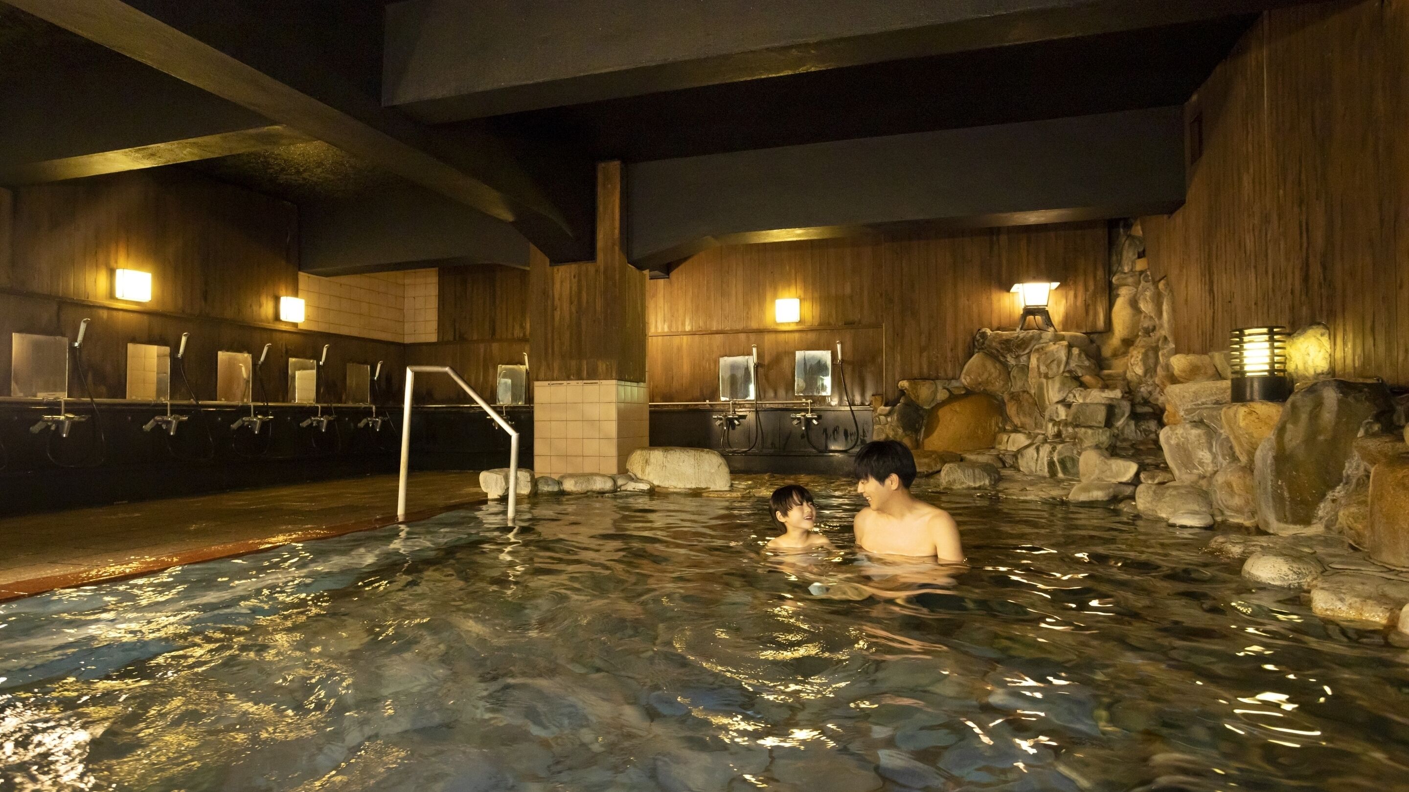 An indoor swimming pool with wooden walls, stone features, and multiple faucets.