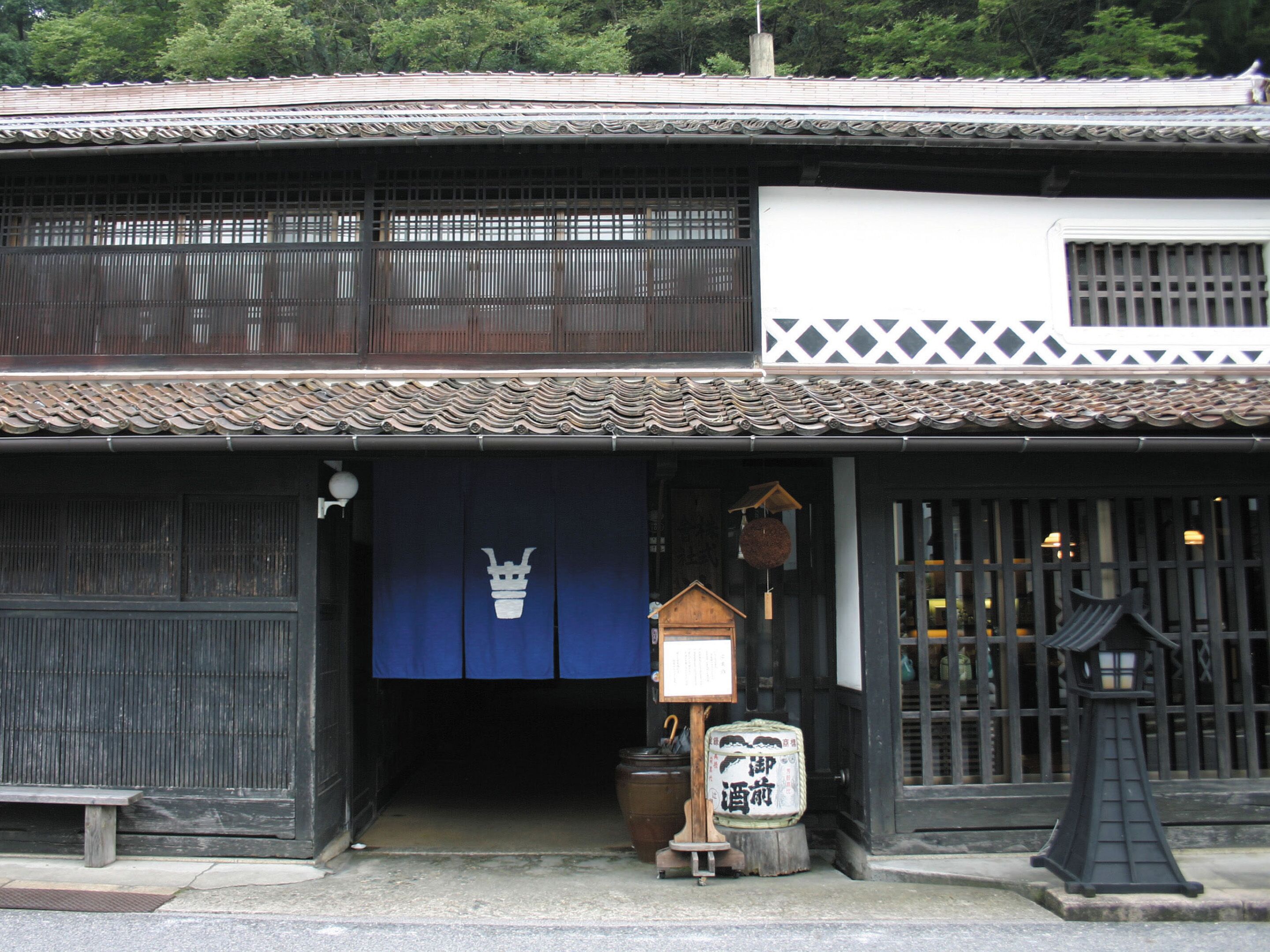 A traditional Japanese building with a dark wooden facade, a tiled roof, and a blue entrance curtain.