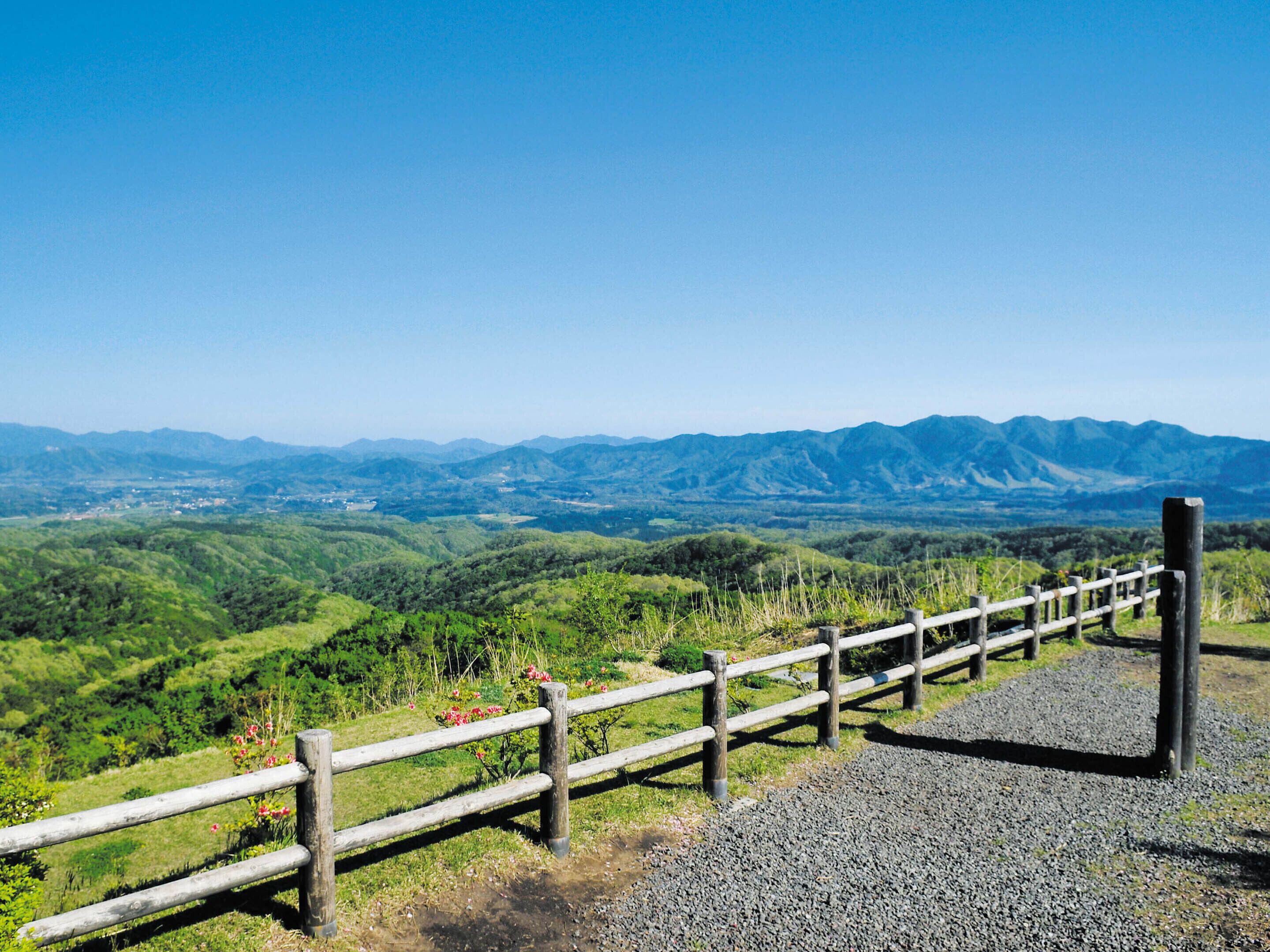 Vista panorâmica de um deck de madeira com um caminho de cascalho, com vista para um vale e montanhas ao longe.