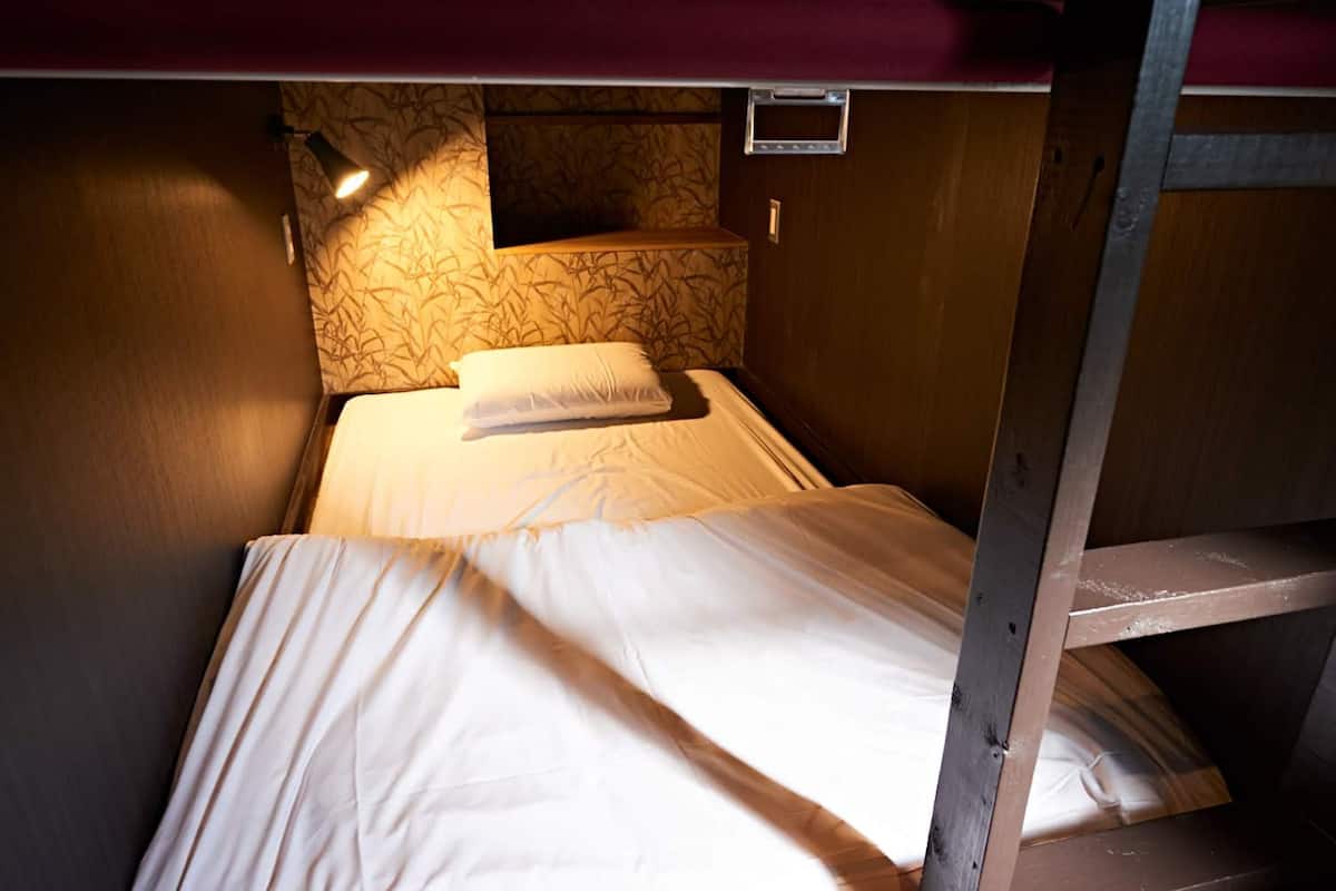 A bunk bed with a mattress and pillows, a headboard with a patterned design, and a small shelf above the bed.