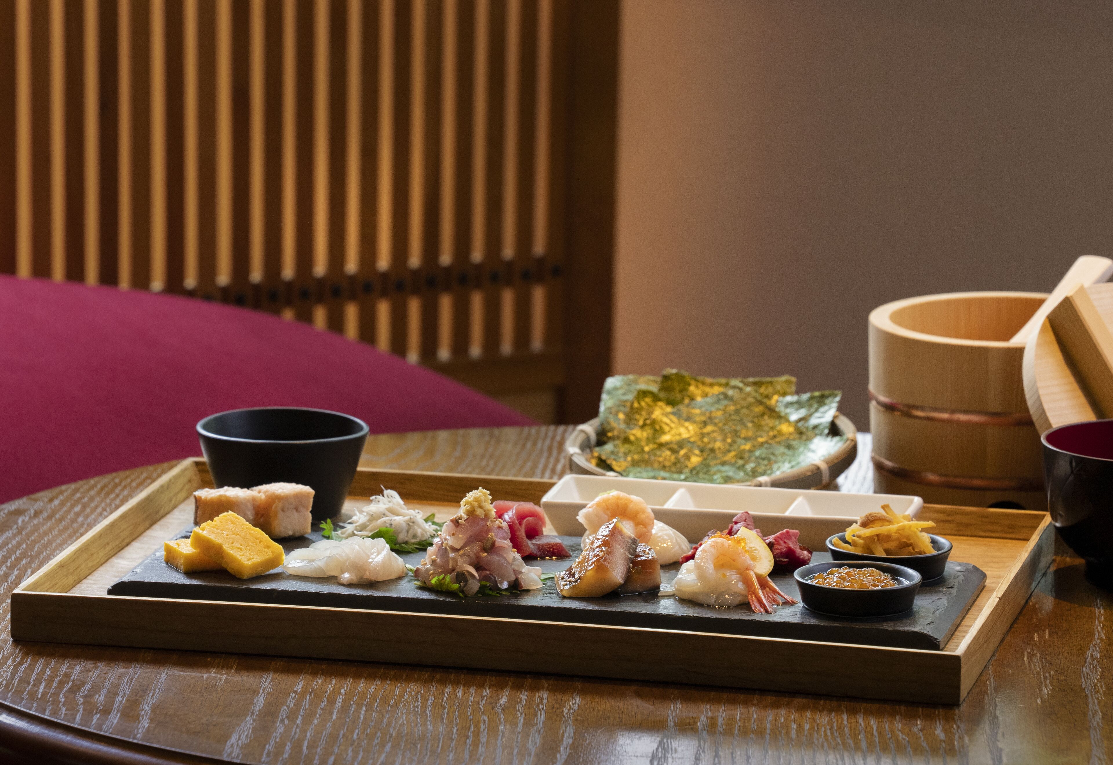 A tray with various sushi and sashimi on a wooden table.
