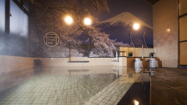 Un bain thermal avec vue sur le mont Fuji, un sol carrelé et une étagère remplie de bouteilles.