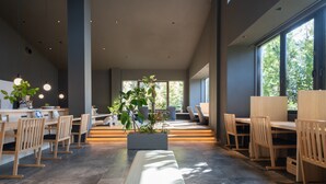 Un intérieur spacieux et moderne, avec de longues tables et des chaises, de grandes fenêtres et une plante au centre.