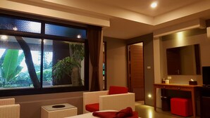 A modern hotel room with a large window, a bed, a desk, and a seating area.