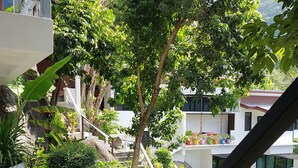 A staircase with a black railing leading to a balcony overlooking a lush garden and a residential area.