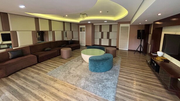 A modern living room with a sectional sofa, ottomans, a round coffee table, and a flat-screen TV. - Extremeli Suites (Parañaque)