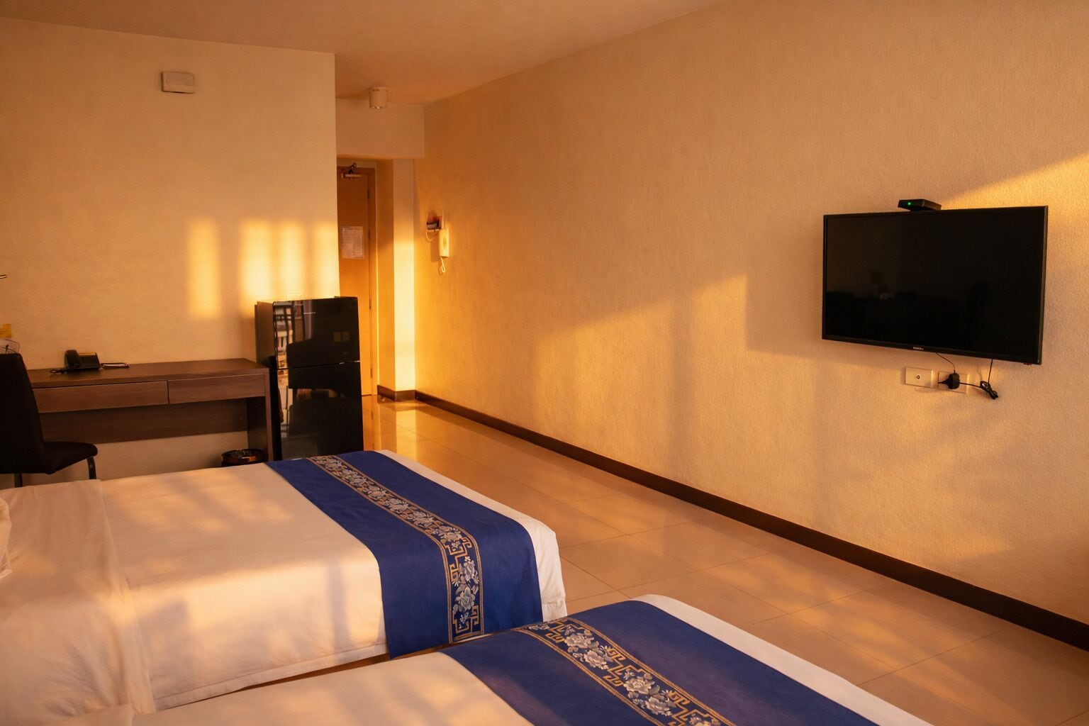 Habitación de hotel con dos camas, un escritorio, una silla, un televisor y un armario.