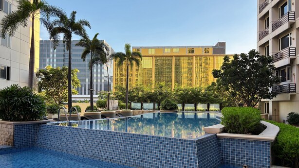 A swimming pool with blue tiles, surrounded by greenery and modern buildings. - Extremeli Suites (Parañaque)